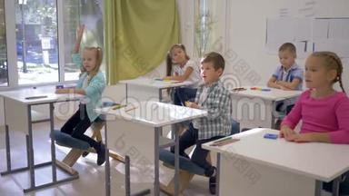 学校里的孩子们，男孩和女孩坐在课桌前，在课堂上举手